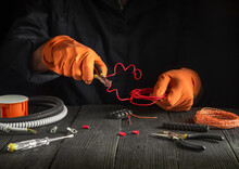 Repair Of Electrical Equipment In The Workshop Of Master Electrician. Close-up Of Gloved Hands Of Electrician Foreman While Working Or Cutting Red Wire