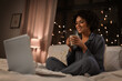 © Syda Productions - technology, bedtime and rest concept - happy smiling woman in pajamas with laptop computer and mug sitting in bed at night and drinking coffee