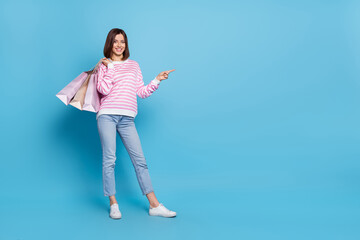 Sticker - Full size photo of cute brunette young lady hold bags index promo wear pullover jeans shoes isolated on blue background