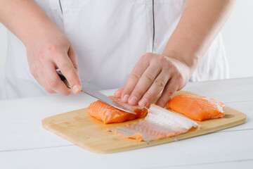 Wall Mural - the chef cuts salmon on a wooden board, on a white background