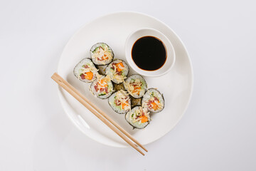 Wall Mural - Sushi with chopsticks on a white plate. Sushi roll japanese food in restaurant isolated on white background. Fresh hosomaki pieces with rice and nori.