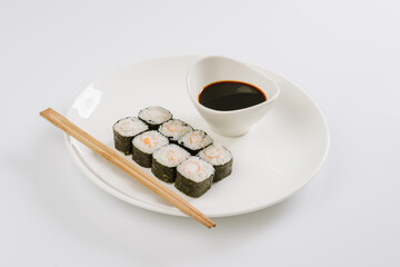 Wall Mural - Sushi with chopsticks on a white plate. Sushi roll japanese food in restaurant isolated on white background. Fresh hosomaki pieces with rice and nori.