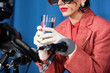 © LIGHTFIELD STUDIOS - partial view of retro style woman in white gloves holding glass of water near blurred microphones on blue background