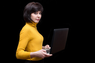 A brunette woman 35-40 years old in a yellow jacket with a high collar with a laptop in her hand on a black background