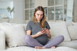 © Татьяна Кочкина - A pregnant woman is sitting on a sofa in the living room with a mobile phone in her hands.