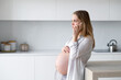 © Татьяна Кочкина - Happy pregnant woman is sitting at home in the kitchen with a mobile phone in her hands.