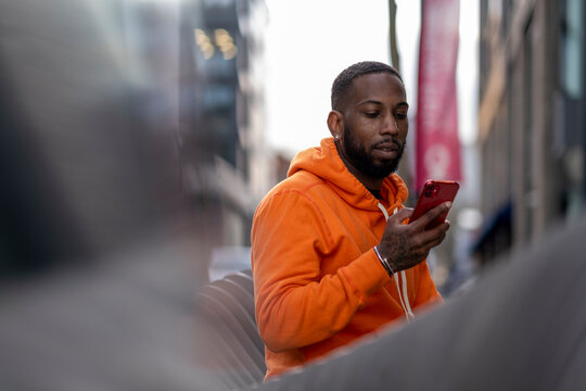 UK, South Yorkshire, Man in orange hooded shirt looking at smart phone in city