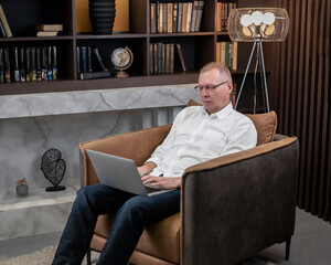 Poster - Business man working at laptop computer on laps, sitting in comfy armchair at home.