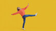 © Studio Romantic - Funny carefree young woman in comfortable casual wear having fun and fooling around. Happy pretty teenage girl in orange sweatshirt and blue jeans dancing in studio with vibrant yellow background