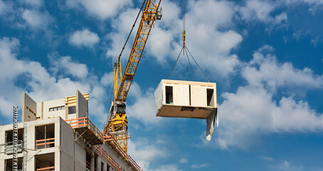 A Crane is lifting a wooden building module to its position in the structure. Construction site of an office building in Berlin, built in modular timber construction.