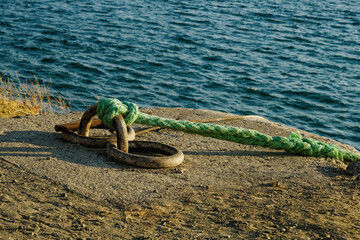 Rusty metal parking barrier with green rope. Old metal bollard for ships in port.