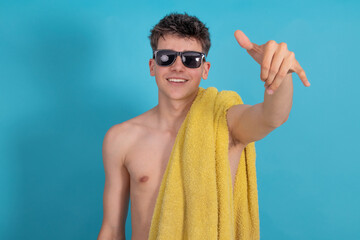 Wall Mural - young man with sunglasses and towel smiling isolated with surfer gesture