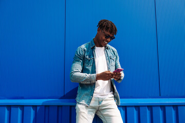 Cheerful african american man holding mobile phone, smiling man using smart phone on blue wall background