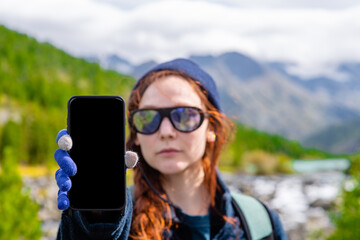 Woman hiker shows empty screen of a smartphone at mountains