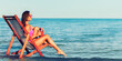 Side view of young woman in pink swimsuit who chilling on the beach while sitting at the deck chair