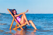 Side view of pretty girl in a pink bathing suit relaxing on the beach while lying at the deck chair