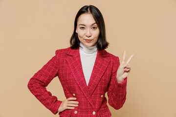 Wall Mural - Happy friendly cool confident fun positive woman of Asian ethnicity wear red jacket showing victory sign isolated on plain pastel beige background studio portrait. People lifestyle fashion concept