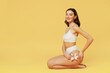 © ViDi Studio - Full size side view young nice beautiful brunette woman 20s wear white underwear sitting on floor hold flower isolated on plain yellow color background studio portrait. People female beauty concept
