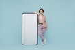 © ViDi Studio - Full body young smiling happy woman 20s wear casual brown shirt stand near big mobile cell phone with blank screen workspace area isolated on pastel plain light blue color background studio portrait
