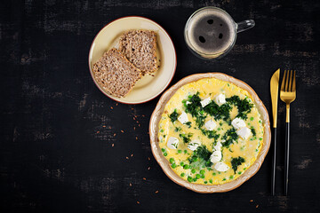 Wall Mural - Healthy breakfast. Omelet with green peas, feta cheese and dill. Dark background. Top view