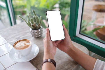 mockup image of a woman holding mobile phone with blank desktop screen in cafe