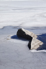 Sticker - A vertical shot of a frozen lake surrounded by rocks under the sunlight in Navacerrada, Spain