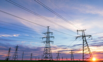 silhouette of high voltage power lines against a colorful sky at sunrise.