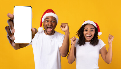 Black couple in santa hats showing white empty smartphone screen