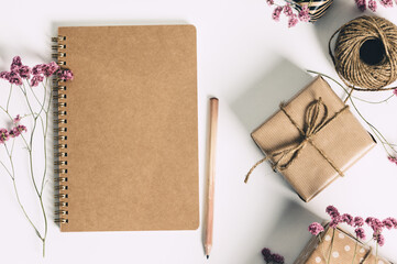 Wall Mural - gift box wrapped in kraft paper, notebook and pink flowers on white background. flat lay styling.