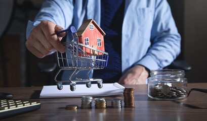 Wall Mural - Real estate agent showing house model over shopping cart and coins.