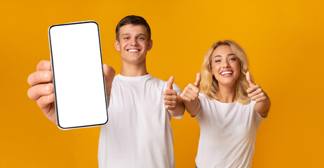 Excited couple showing empty smartphone screen and thumbs up