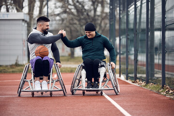 Happy athletes with disabilities greet while playing wheelchair basketball on the outdoor court.