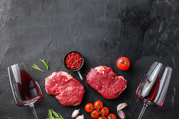 Wall Mural - Raw rump steaks from organic beef meat cuts near red wine glasses with rosemary, garlic and spices over black textured  background, top view with space for text.