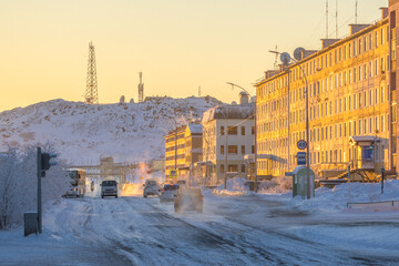 Wall Mural - Street in a northern city in the Arctic. Winter city landscape. Cars drive along a snow-covered street. Buildings at sunset. Telecommunication towers on the mountain. Anadyr, Chukotka, Siberia, Russia