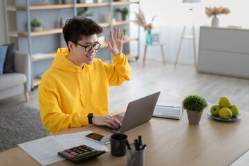 Wall Mural - Smiling asian man working on laptop waving hand