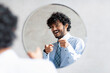 © Prostock-studio - You're handsome. Confident indian businessman pointing at mirror in bathroom with two fingers, wearing shirt and smiling
