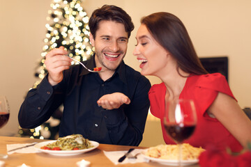 Wall Mural - Smiling guy feeding his woman with pasta