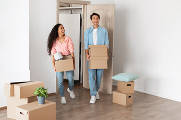 Poster - Happy couple holding cardboard boxes, walking in new house