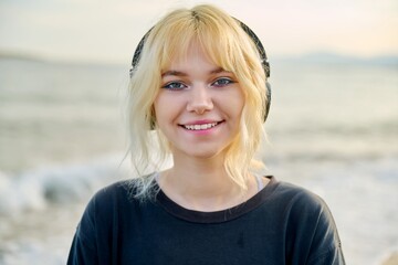 Poster - Portrait of smiling teenage female wearing headphones, on beach, close-up face, smile with teeth