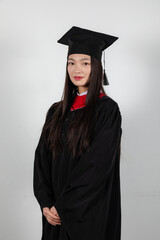Wall Mural - Smiling graduate student in mortar board and bachelor gown on white background