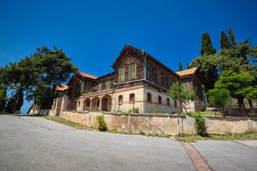 Wall Mural - An old house made of stone and wood, trees and pine trees grow nearby. Old orthodox monastery. Travel to Buyukada, Adalar, Prince Islands, Istanbul, Turkey