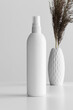 White cosmetic spray bottle mockup with a dry flower on the white table.