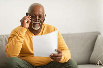 Contented Senior Black Man Reading Papers Wearing Eyeglasses At Home