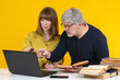 Student and tutor on yellow. Man tutor teaches girl. Guy and girl are sitting in front of laptop. Gray-haired teacher is engaged in tutoring. Teacher helps student prepare for exam. Teaching career
