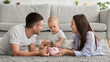 © Prostock-studio - Financial Literacy. Infant Boy Putting Coins To Piggy Bank, Relaxing With Parents