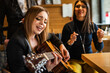 © Miljan Živković - Front view portrait of adult caucasian woman sitting at cafe with guitar on her lap looking to the hand holding accord singing to her friends - female musician relaxed real people leisure concept