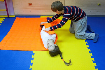 boy and girl children roll each other up in a thick blanket on mats controlling a small space for autism treatment in a correctional center