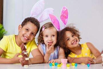 Wall Mural - three children in bright clothes eating Easter eggs