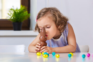 Wall Mural - Girl kissing Easter chocolate bunny sitting at home