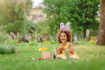 Little Black girl wtfring bunny ears gathering Easter eggs